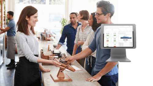 Two restaurant staff using a touchscreen POS system in a commercial kitchen environment